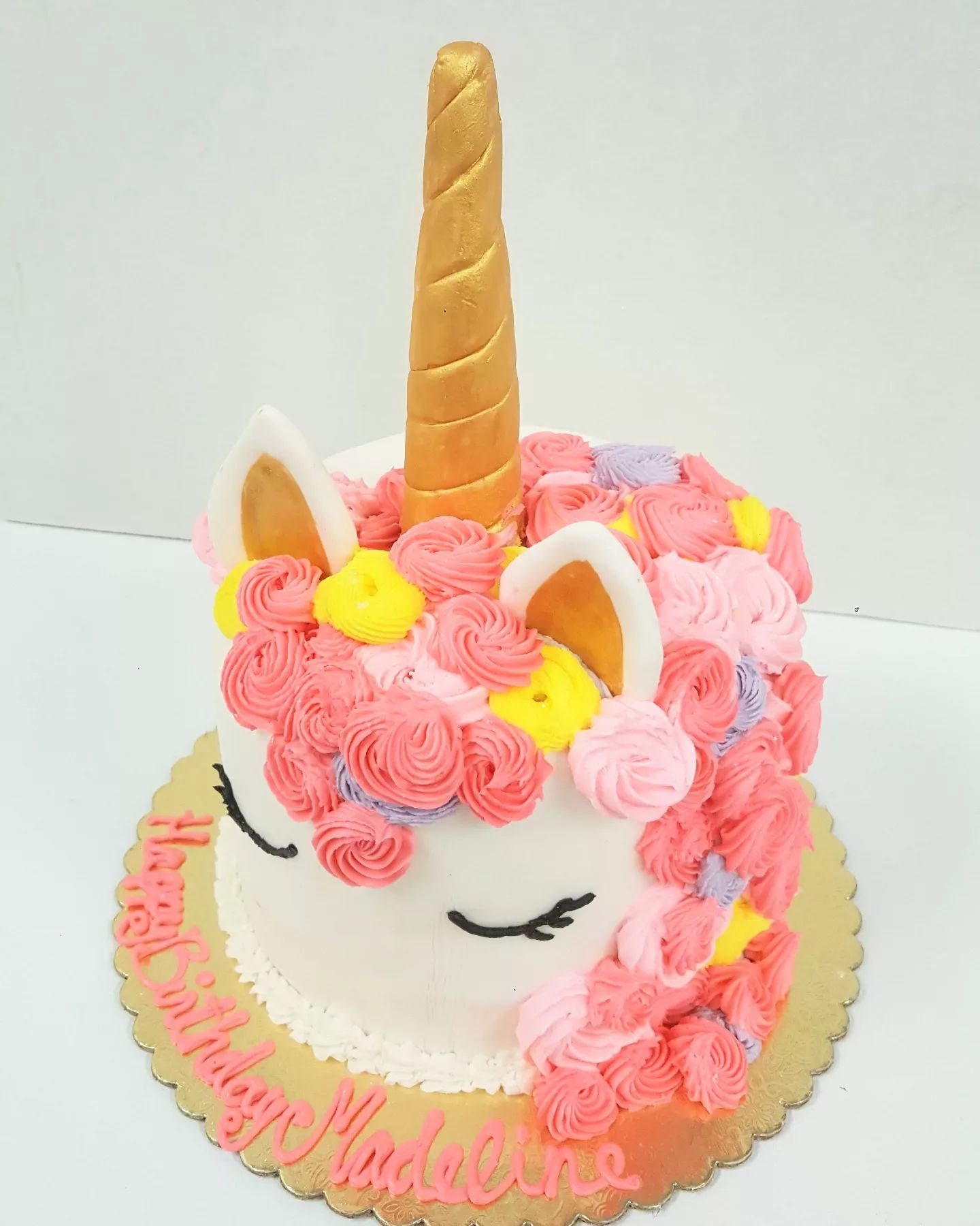 unicorn head cake with a gold horn and ears decorated with buttercream